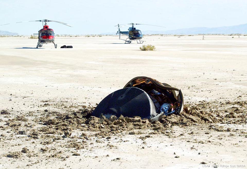 Prezentowane zdjęcie ukazuje zakopany w piasku dysk misji NASA Genesis oraz widoczne w oddali dwa helikoptery. 
Więcej szczegółowych informacji w opisie poniżej.