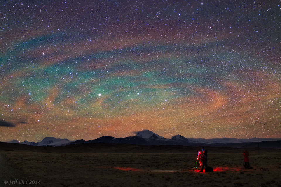 Opisywane zdjęcie pokazuje ciemne pole z oświetlonym
czerwonym światłem fotografem wykonującym zdjęcie nocnego nieba
zabarwionego zieloną poświatą i udekorowanego chmurami, które
wspólnie wyglądają jak olbrzymia spirala.
Zobacz opis. Po kliknięciu obrazka załaduje się wersja
 o największej dostępnej rozdzielczości.