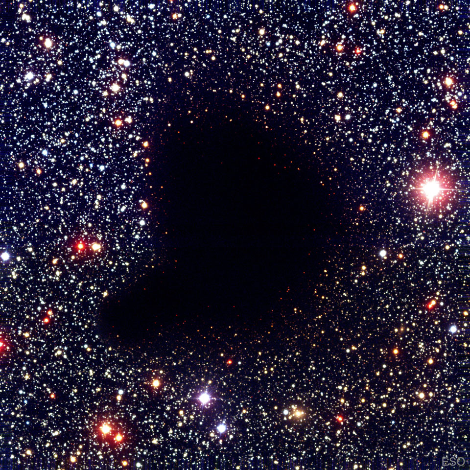 A dark comma-shaped cloud appears in the middle of a dense
field of stars. No stars are visible through the center of the cloud.
Please see the explanation for more detailed information.