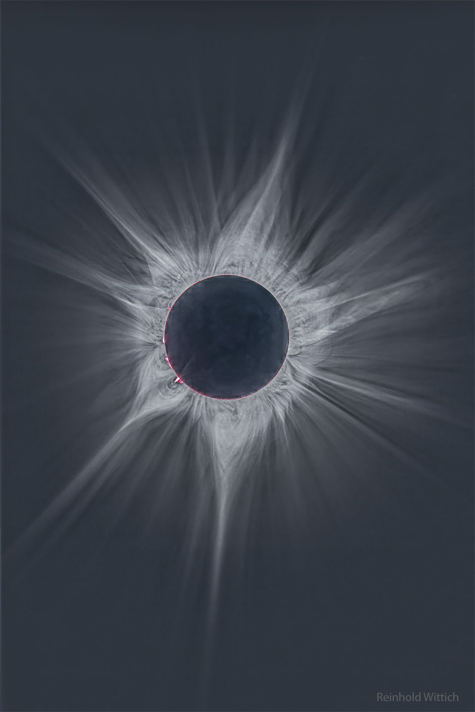 Obraz przedstawia głębokie ujęcie otaczającej Słońce korony
podczas zaćmienia całkowitego z kwietnia 2023 r. Tarcza centralna
jest ciemna, a z niej wydaje się wychodzić wiele skomplikowanych jasnych
promieni. Wokół krawędzi Słońca można dostrzec kilka gorących różowych
włókien. Zobacz opis. Po kliknięciu obrazka załaduje się wersja
 o największej dostępnej rozdzielczości.