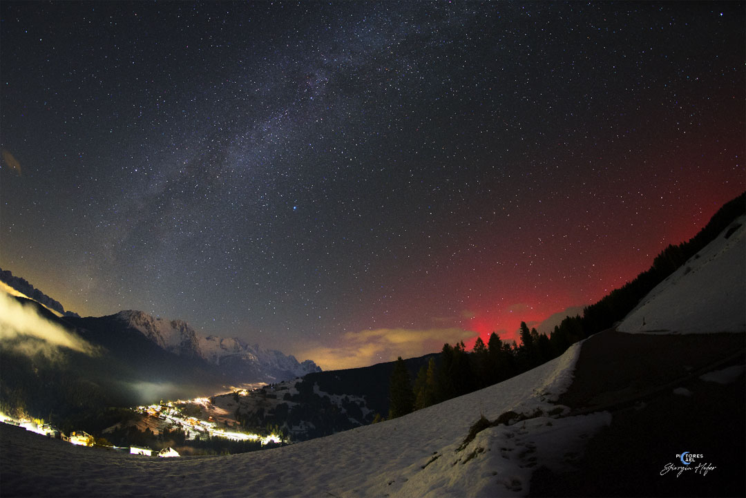 Na zdjęciu pokazano nocne niebo nad doliną, wypełnione
centralnym pasem Drogi Mlecznej, przecinającej je po przekątnej
od dolnego lewego rogu. Po prawej stronie nieba tuż nad wzgórzem
świeci niezwykła czerwień: zorza polarna. Zobacz opis. Po kliknięciu obrazka załaduje się wersja
 o największej dostępnej rozdzielczości.