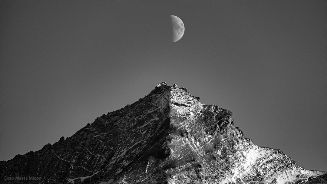 Na zdjęciu przedstawione są czarno-białe obrazy Księżyca oraz góry.
Oba obiekty są w połowie oświetlone przez Słońce. Drugie połowy kryją się w cieniu. Połowa Księżyca widoczna jest 
dokładnie nad szczytem góry.
Więcej szczegółowych informacji w opisie poniżej.