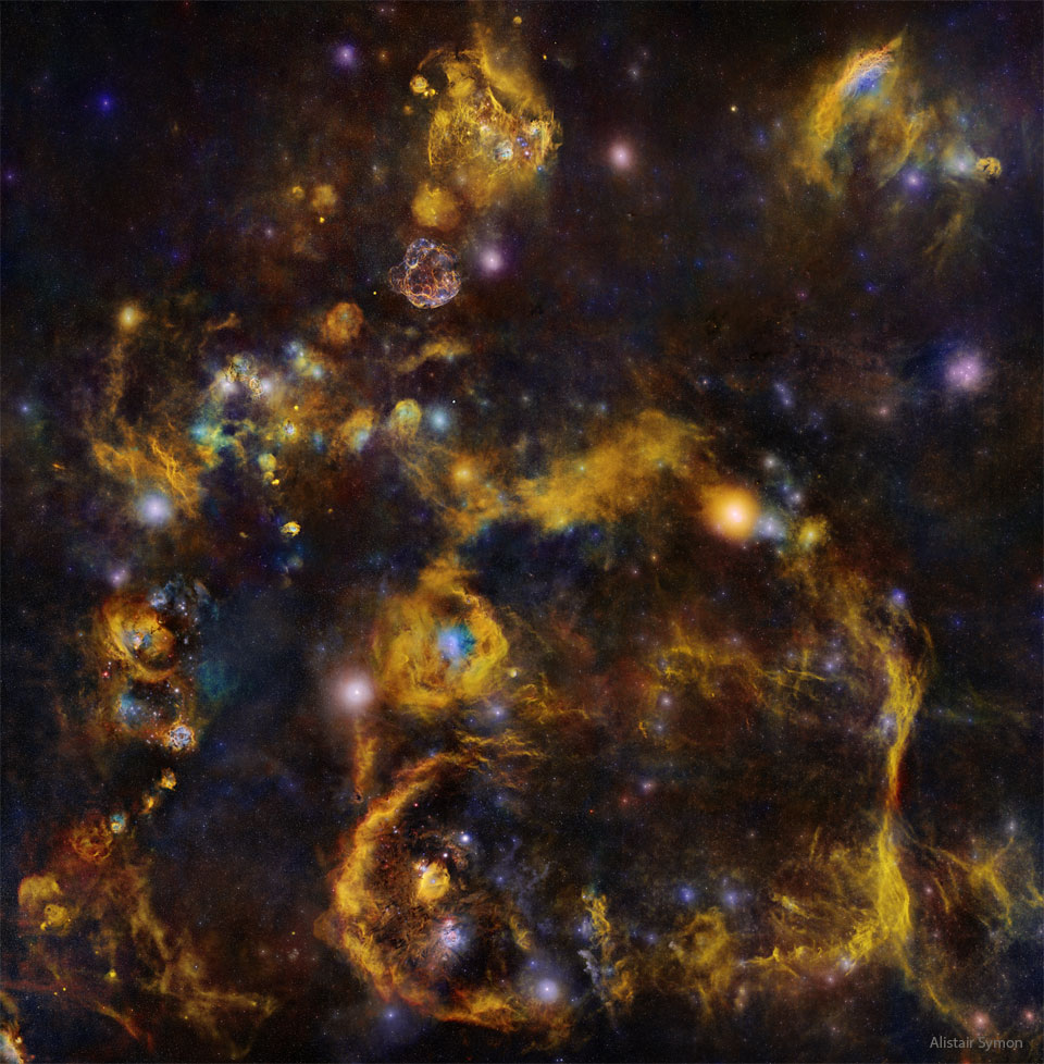 Bardzo głębokie zdjęcie nocnego nieba pokazuje wiele gwiazd i mgławic.
Duża część z nich wydaje się łączyć ze sobą poprzez słabe pomarańczowe włókna.
Zobacz opis. Po kliknięciu obrazka załaduje się wersja
o największej dostępnej rozdzielczości.