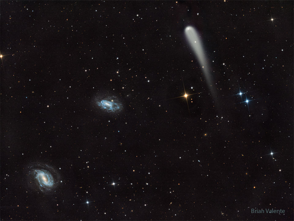 A picture shows a starfield with three prominent objects.
A blue spiral galaxy is on the lower left and another blue spiral
is just left of center. Toward the upper right is a light-colored
comet with a tail fading toward in the image bottom.
Więcej szczegółowych informacji w opisie poniżej.