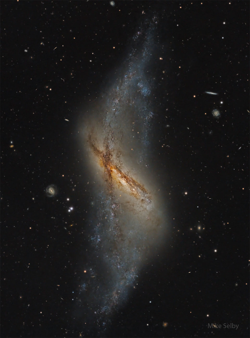 A dark starfield has an unusual galaxy in the center.
This galaxy has a spindle-like shape showing two dust
lanes -- one running vertically and one running diagonally
from the upper left. 
Więcej szczegółowych informacji w opisie poniżej.