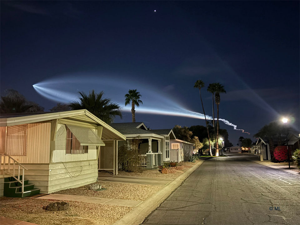 Houses are seen on a street below the night sky.
In the sky is a bright light plume that looks like the outline
of a giant fish. 
Więcej szczegółowych informacji w opisie poniżej.