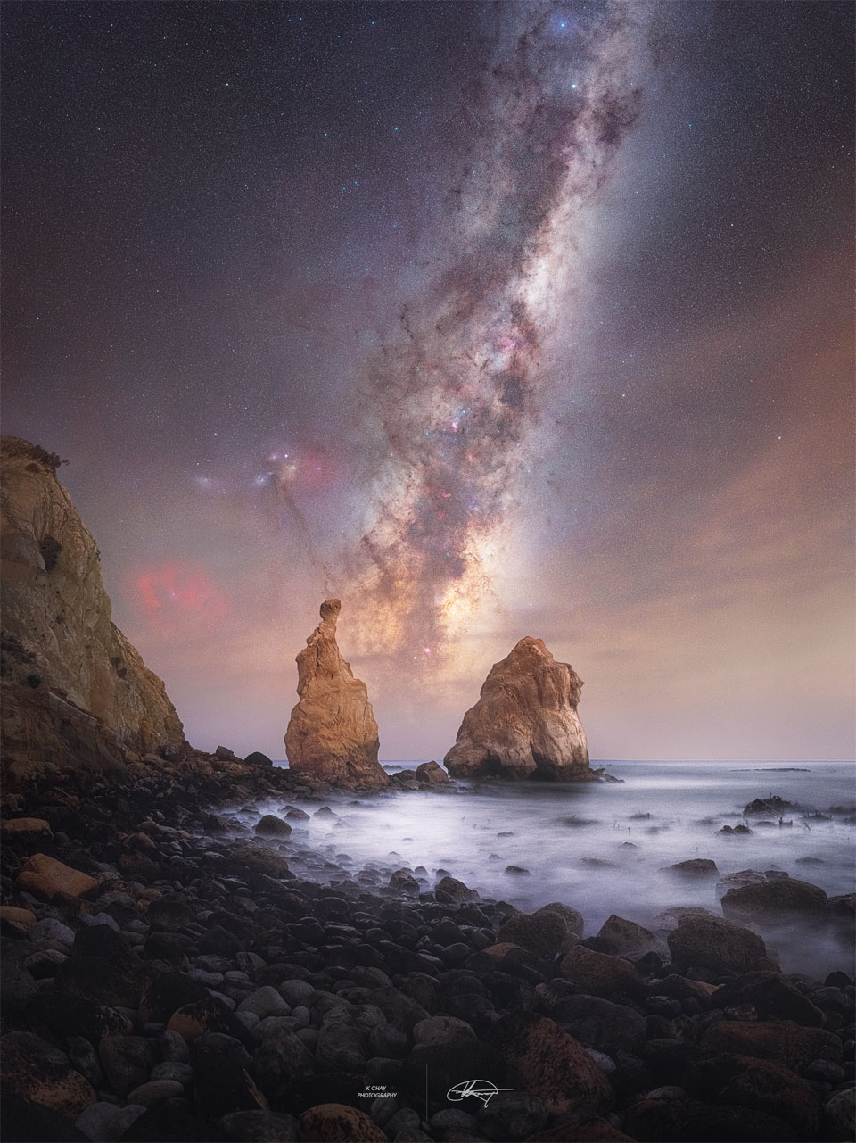 A skyscape is seen above an water inlet.
Two rock spires rise from the sea, and the central
band of our Milky Way Galaxy is seen between them.
Więcej szczegółowych informacji w opisie poniżej.