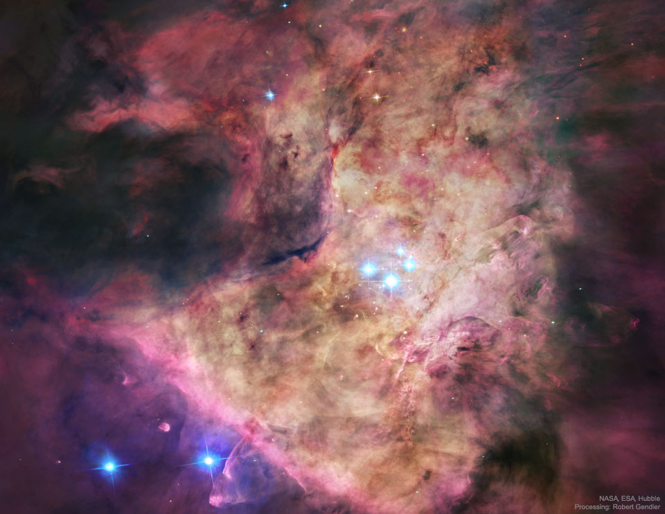 A bright nebula occupies the center of the frame. 
The nebula is complex but roughly tan in the center and
red around the edges. In the center are four bright blue stars.
Więcej szczegółowych informacji w opisie poniżej.