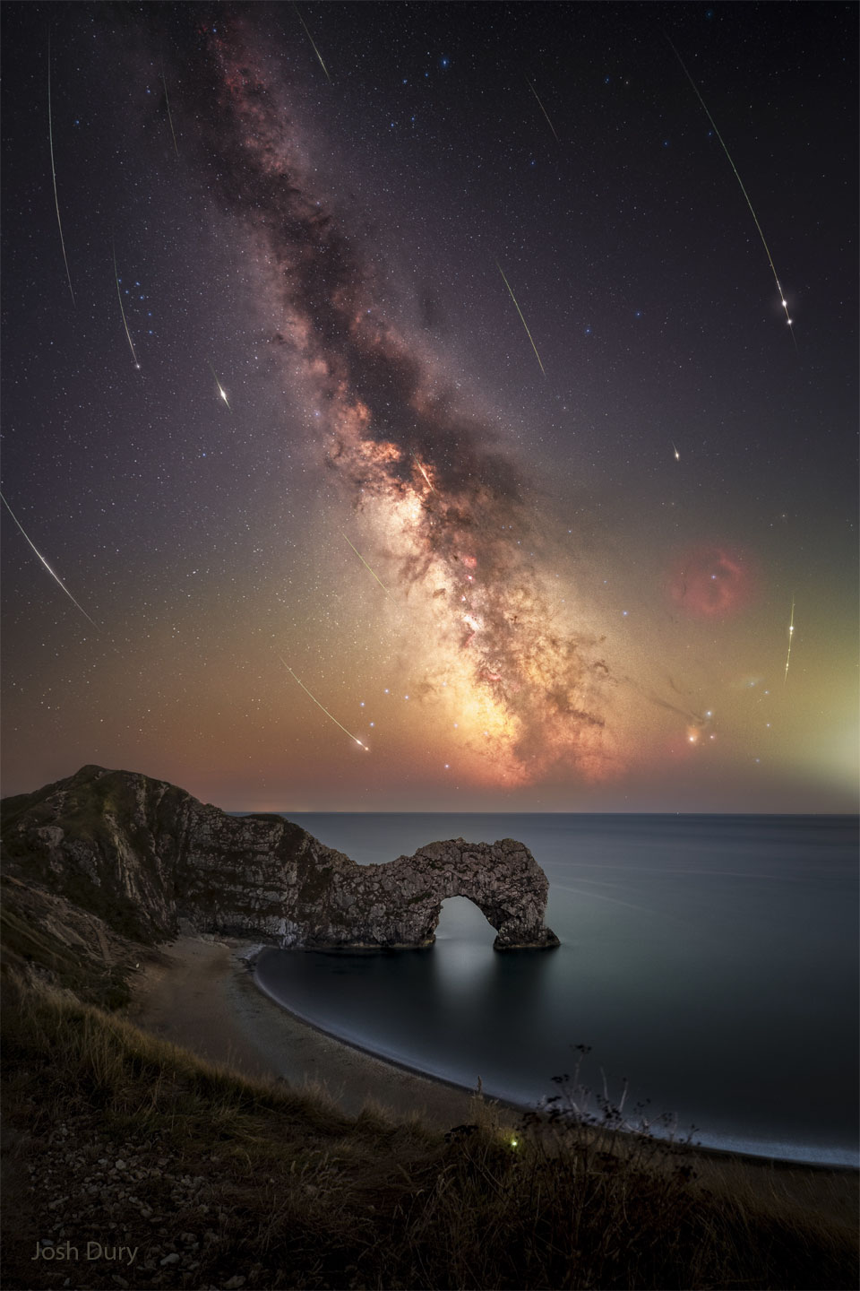 A deep sky is shown with the band of our Milky Way Galaxy
running from the upper left to the lower right. The streaks
or many curved meteors are seen. In the foreground a beach
is seen with an unusual rock outcrop that has an opening.
Więcej szczegółowych informacji w opisie poniżej.